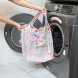 A person holds a bag from Bumkins The Playdate Planner Deluxe 5-Piece Set: Boots in front of an open front-loading washing machine.