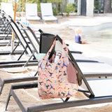 Beach chairs by a pool with a Bumkins Packable Tote Bag: Yoga Pals hanging on one. A child plays near the water in the background.