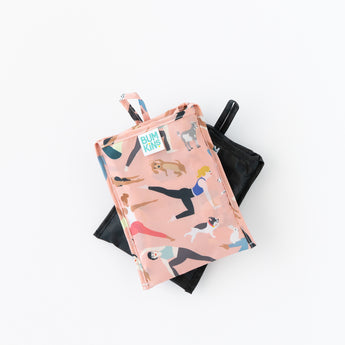 Bumkins Packable Tote Bag: Yoga Pals, folded in its pocket, is shown stacked on top of another bag on a white background.