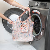 A person holds Bumkins Yoga Pals Packable Tote Bag in front of an open front-loading washing machine.