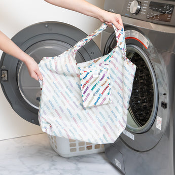 A person holds a bag from Bumkins The Playdate Planner Deluxe 5-Piece Set: Mickey & Friends Varsity in front of an open washing machine.
