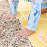 Close-up of a child playing with sand on a Bumkins Reversible Roll & Go Blanket, Desert Boho, wearing a blue abstract long-sleeve.