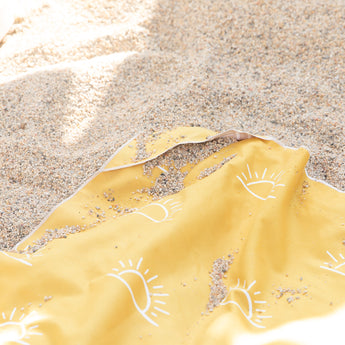 Close-up of Bumkins Reversible Roll & Go Blanket, Desert Boho covered in sand on a beach.