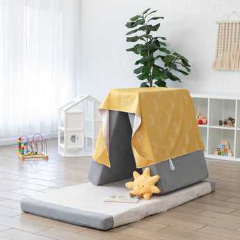 A play area features gray cushions with Bumkins Reversible Roll & Go Blanket, Desert Boho draped over the top, with a plush sun in front.