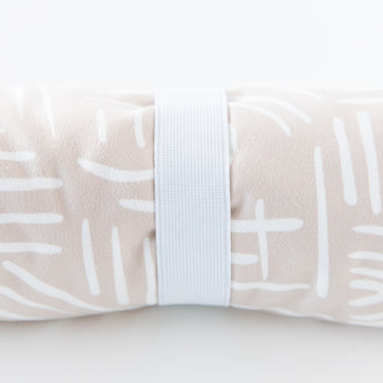 Close-up of a rolled Bumkins Reversible Roll & Go Blanket, Desert Boho on a white background, secured by a white elastic band.