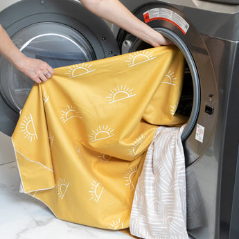 A person loads a Bumkins Reversible Roll & Go Blanket, Desert Boho into an open front-loading washing machine.