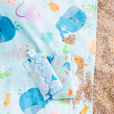 Close-up of Bumkins Reversible Roll & Go Blanket, Rolling with the Waves with small bags on a sandy beach.