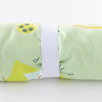 Close-up of a rolled Bumkins Reversible Roll & Go Blanket, Happy Camper on a white background, secured by a white elastic band.