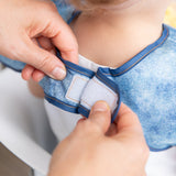 Close-up of adult hands adjusting the closure of a bib from Bumkins Snack In Style 3-Piece Set: Denim On Denim around a child's neck.