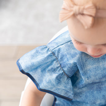 Close-up of a young girl in a bib from Bumkins Snack In Style 3-Piece Set: Denim On Denim.