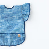 Bumkins Ruffle Apron Bib: Crushed Denim lays flat on a white background.