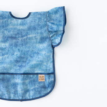 Bumkins Ruffle Apron Bib: Crushed Denim lays flat on a white background.