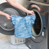 A person holds Bumkins Ruffle Apron Bib: Crushed Denim in front of an open front-loading dishwasher.