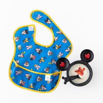 Bumkins Silicone First Feeding Set: Mickey Mouse Classic Black with yogurt & berries rests next to a yellow & blue bib on a white background.