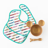 Bumkins Silicone First Feeding Set: Minnie Mouse Gold rests on a white background next to a colorful Disney-themed bib.