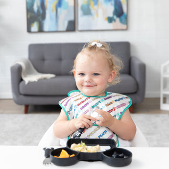A young girl smiles as she enjoys a meal with Bumkins On-The-Go Mealtime 7-Piece Set: Mickey & Friends MVP.