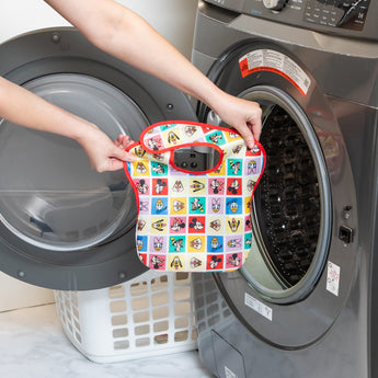 A person holds a Bumkins SuperBib® 3 Pack: Mickey & Friends MVP in front of an open front-loading washing machine.