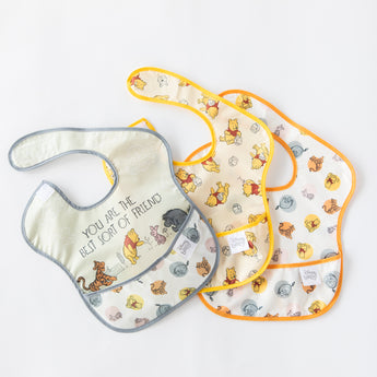 Bibs from Bumkins On-The-Go Mealtime 7-Piece Set: Pooh Bear + Friends lay overlapped on a white background.