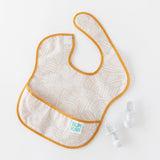 Bumkins Silicone Chewtensils®: Marble rest next to a beige patterned bib on a white background.