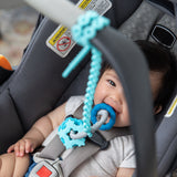 A smiling child chews a Bumkins Silicone Teething Charms: Blue attached to a blue silicone tether in a car seat.