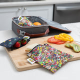 Bumkins Reusable Snack Bag, 3-Pack: Super Mario™ Power Up holds a sandwich & berries on a kitchen counter by an open lunch bag.