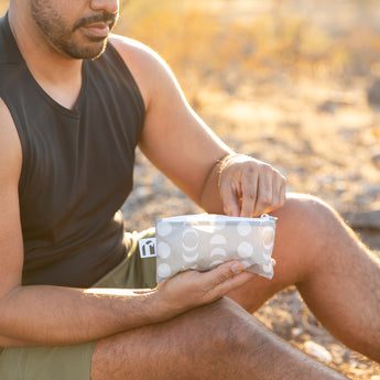 A man eats snacks from a bag from Roamio by Bumkins Reusable Snack Bag 4 Pack: Desert Night in golden sunlight.