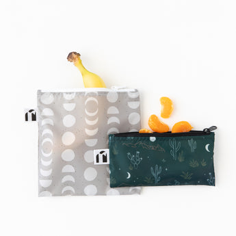 Two bags from Roamio by Bumkins Reusable Snack Bag 4 Pack: Desert Night hold fruit on a white background.