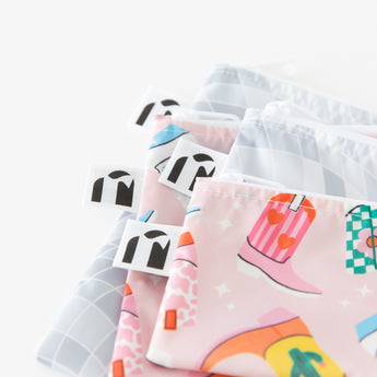 Close-up of Roamio by Bumkins Snack Bag 4 Pack: Disco Boots stacked on a white background, with focus on the zippers and logo tags.