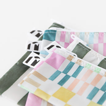 Close-up of Roamio by Bumkins Snack Bag 4 Pack: Motley Club stacked on a white background, with focus on the zippers and logo tags.