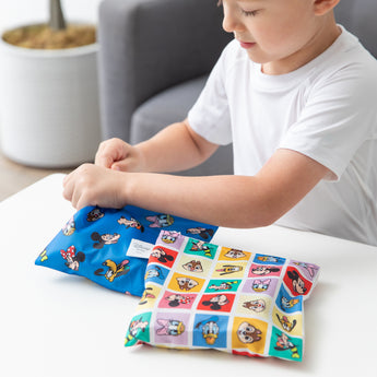 A child holds a Bumkins Snack Bag 4 Pack: Mickey & Friends Excellent Eight at a white table.