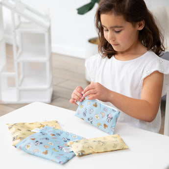 A young girl opens Bumkins Snack Bag 4 Pack: Mickey + Minnie Mouse Brunch Bunch at a white table in a bright playroom.