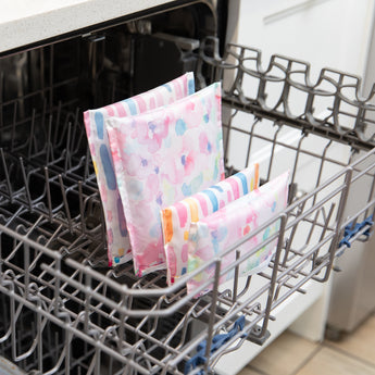 Bumkins Reusable Snack Bag 4 Pack in Watercolor & Brushstrokes stands upright in the bottom rack of an open dishwasher.
