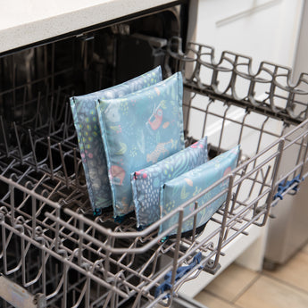 Bumkins Reusable Snack Bag 4 Pack in jungle and animal prints is placed on the dishwasher’s bottom rack for cleaning.