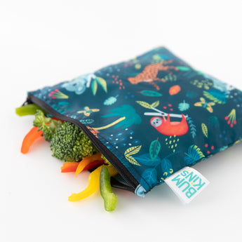 Fresh veggies spill from an open Bumkins Reusable Snack Bag, Large 2-Pack: Jungle & Animal Prints on a white background.