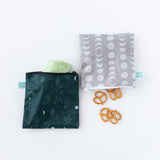 Bumkins Reusable Snack Bag, Large 2 Pack: Desert Night lays on a white background, one bag with a wrap and the other with pretzels.