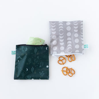 Bumkins Reusable Snack Bag, Large 2 Pack: Desert Night lays on a white background, one bag with a wrap and the other with pretzels.