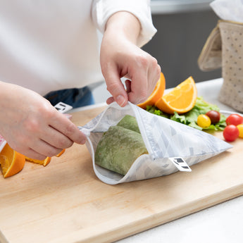 Close-up of a person packing a wrap in a bag from Bumkins Snack In Style 3-Piece Set: Disco Boots on a cutting board with fruit & veggies.