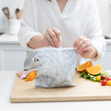 A person zips a bag from Bumkins Snack In Style 3-Piece Set: Disco Boots on a cutting board with fruit and veggies.