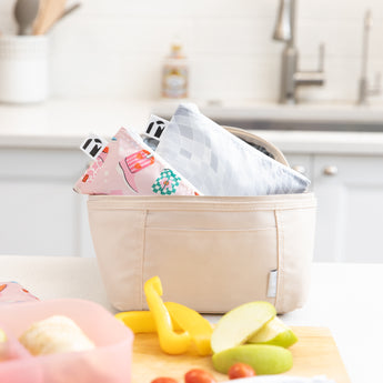 Bags from Roamio by Bumkins Snack Bag 4 Pack: Disco Boots sit inside a beige lunch bag on a kitchen counter by fruit & veggie slices.