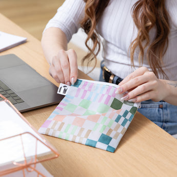 A person opens a Roamio by Bumkins Reusable Snack Bag, Large 2 Pack: Motley Club at a desk next to a laptop and papers.