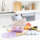 A kitchen counter with Bumkins Lunchbox Legends 6-Piece Set: Coastal Purple Jelly, lunch bag, cutting board, and fruit & veggies.