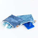 Roamio by Bumkins Reusable Snack Bag, Large 2 Pack: Denim on Denim lays open on a white background with camera cleaner & a charger inside.