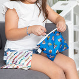 A child wearing a white shirt on a couch zips Bumkins Reusable Snack Bag, Large 2 Pack: Mickey & Friends MVP.