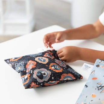 A child zips a bag from Bumkins Snack In Character 3-Piece Set: Disney Everyday Is Halloween Jack on a white table.