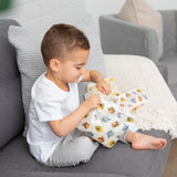 A boy sits on a gray couch with Bumkins Reusable Snack Bag 4 Pack: Disney Pooh Bear + Friends next to a cream blanket and light gray pillow.