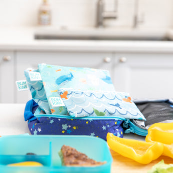 Bumkins Reusable Snack Bag 4 Pack: Ocean Life & Whale Tail sits in an open lunch bag on a kitchen counter by pepper slices and a bento box.