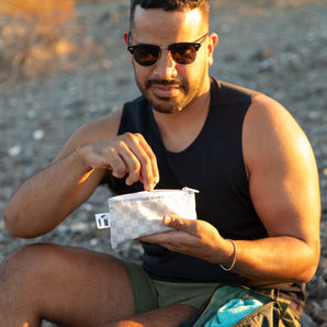 A man in sunglasses reaches into a Roamio by Bumkins Reusable Snack Bag, Small 2 Pack: Rich & Boujee outdoors in golden sunlight.