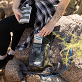 A person packs Roamio by Bumkins Reusable Snack Bag, Small 2 Pack: Motley Club in a backpack outdoors on rocks.