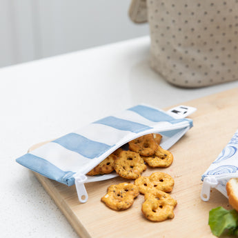 A Bumkins Reusable Snack Bag, Small 2 Pack: Coastal holds pretzels on a wood cutting board on a kitchen counter.
