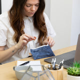 A woman eats a snack from a Roamio by Bumkins Reusable Snack Bag, Small 2 Pack: Denim on Denim at a desk with a laptop, notepad, and pens.